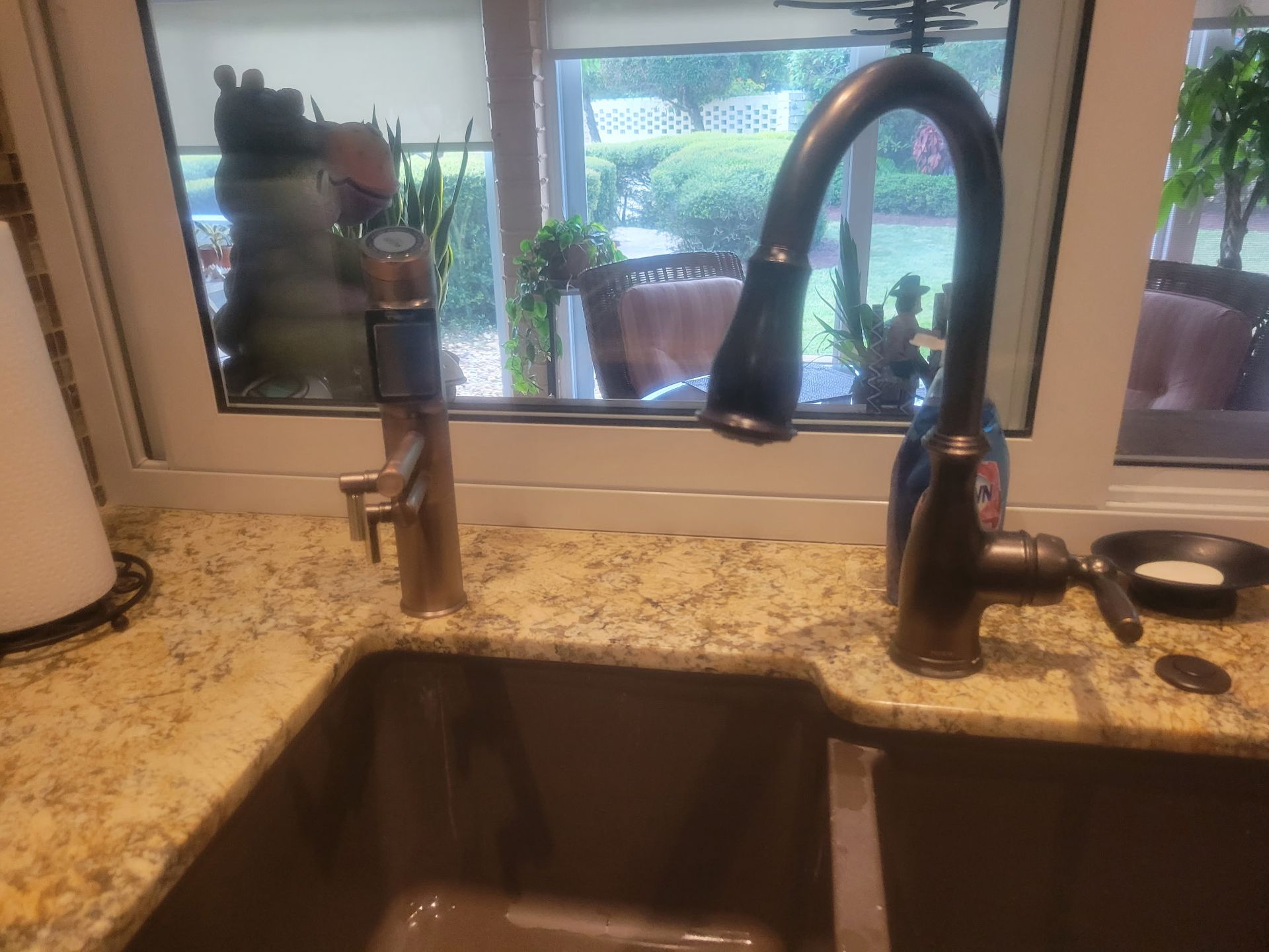 Kitchen sink with granite countertop, black faucet, and window view of patio and greenery.