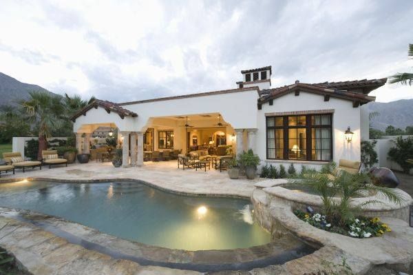 A luxury stucco home with a terracotta roof, open patio, and a stone-trimmed swimming pool against a mountain backdrop.