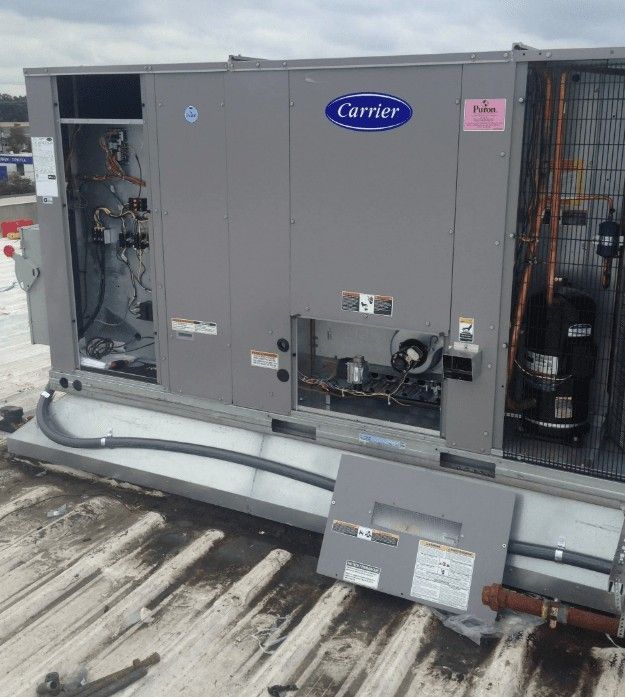 A gray industrial Carrier HVAC rooftop unit with open service panels, resting on a flat, weathered commercial roof.