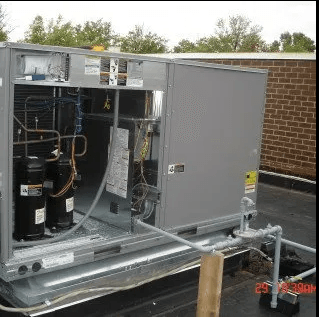 A large HVAC rooftop unit with exposed interior components and external piping on a flat roof.