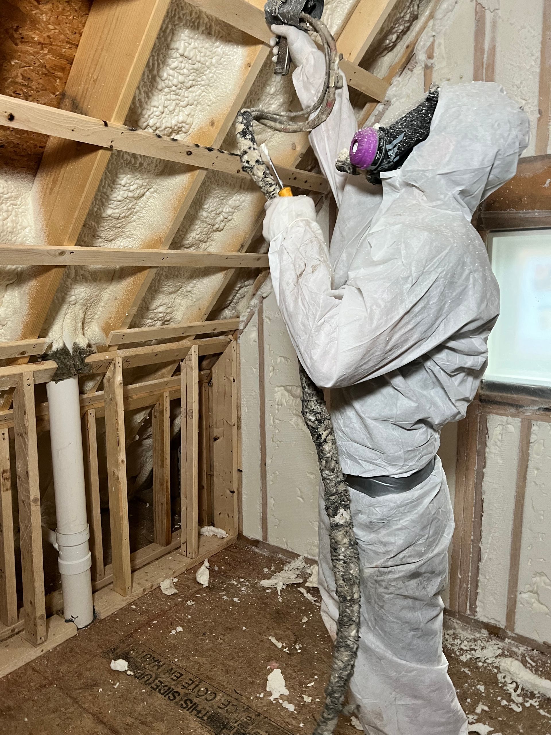 A man is spraying insulation on the ceiling of a room.