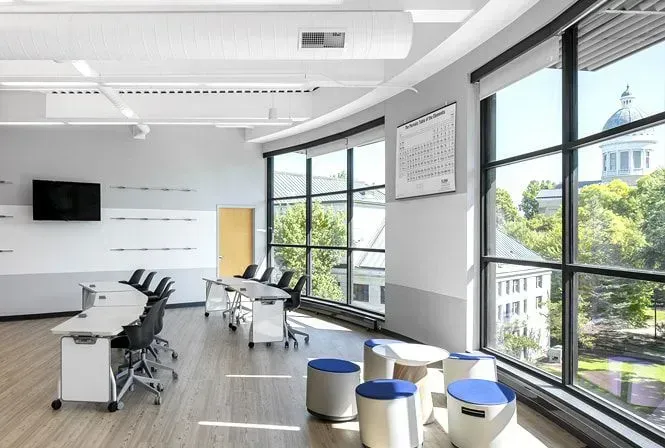 Modern classroom with curved windows and city views. Tables and chairs arranged for learning.