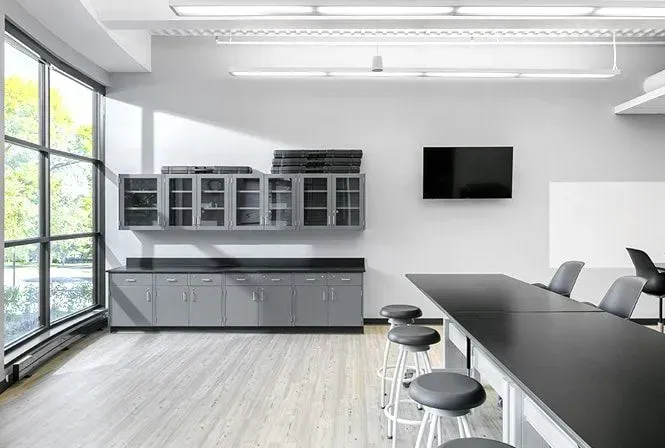Modern laboratory: gray cabinets, long black table with stools, large window, TV, and whiteboard.