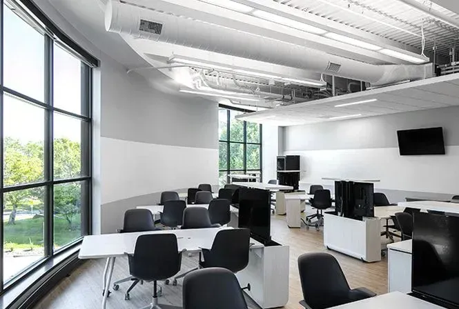 Modern office with large windows, white walls, desks, and black chairs.