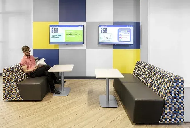Man reading in a modern lounge with two screens on a color-blocked wall.