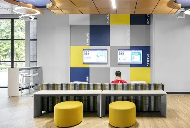 Modern office space with colorful wall, screens, and seating. Person seated at desk.