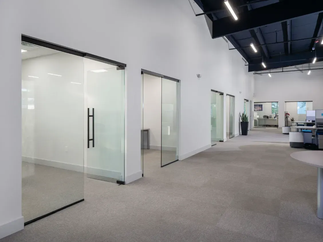 Office hallway with glass sliding doors, gray carpet, white walls, and dark ceiling.