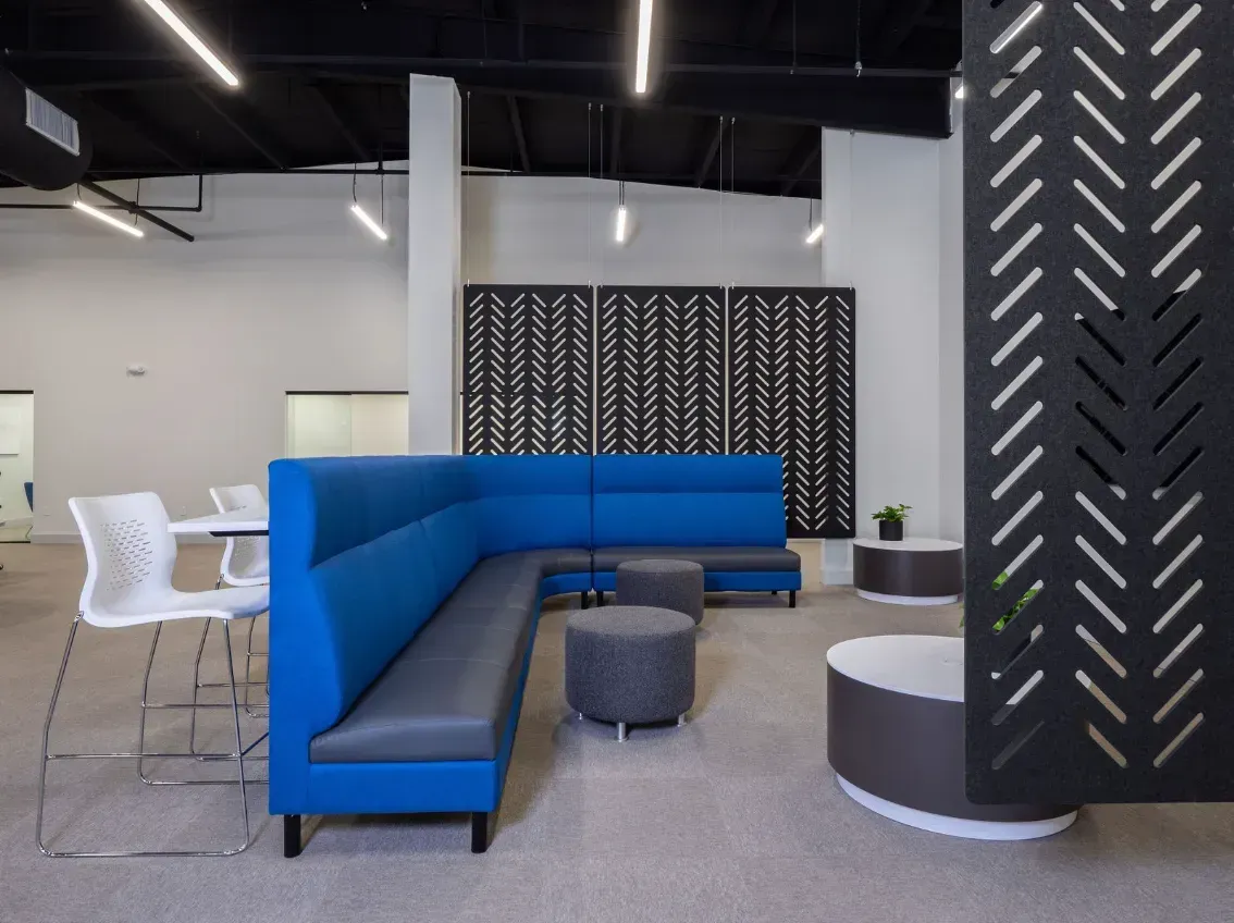 Modern office space with blue sectional sofa, gray ottomans, decorative screen, and round tables.