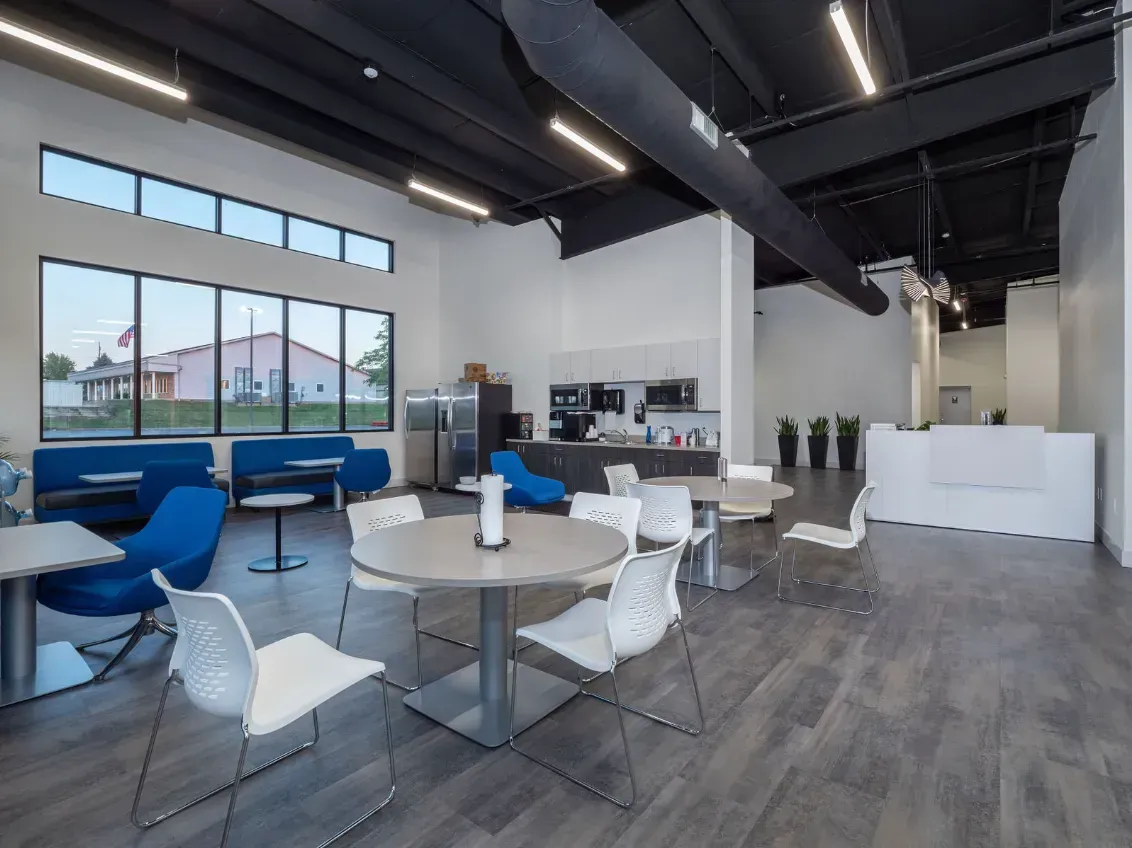 Interior of a modern cafe with tables, chairs, and a seating area; large windows.