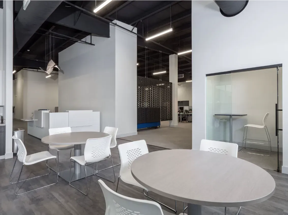 Modern office interior with round tables, white chairs, and glass-walled office space.