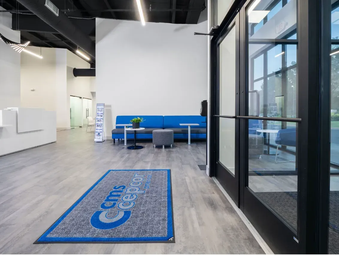 An office lobby with a blue couch, welcome mat, and glass doors.