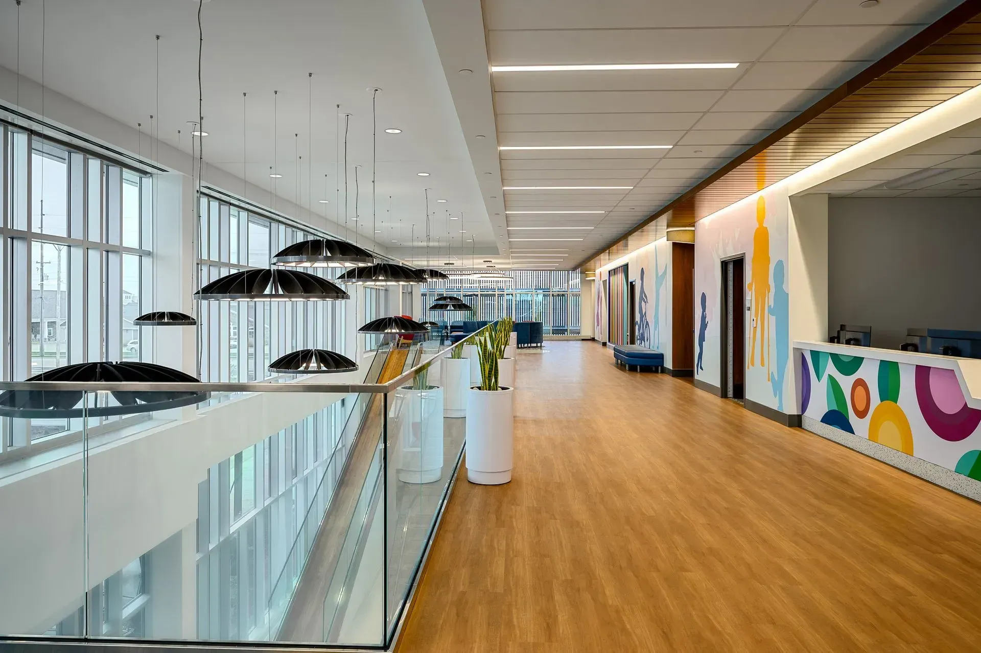 Hallway with glass railing, modern light fixtures, wood floor, and colorful artwork.