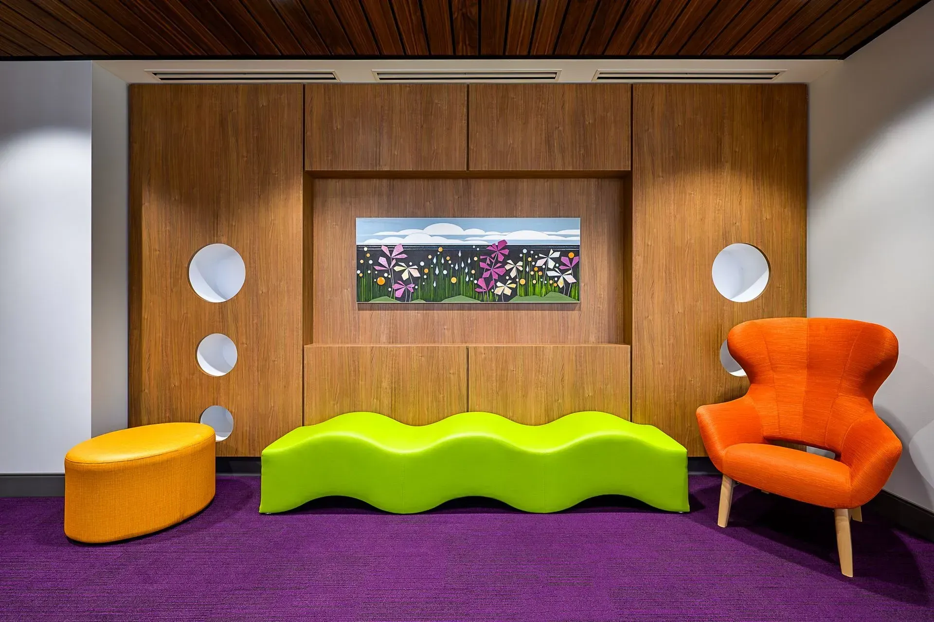 Playroom with wood paneling, colorful seating, and a nature scene display. Purple carpet.