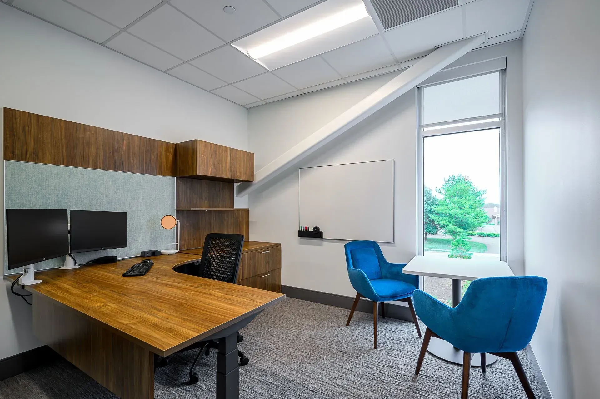 Modern office with wooden desk, blue chairs, whiteboard, and window.