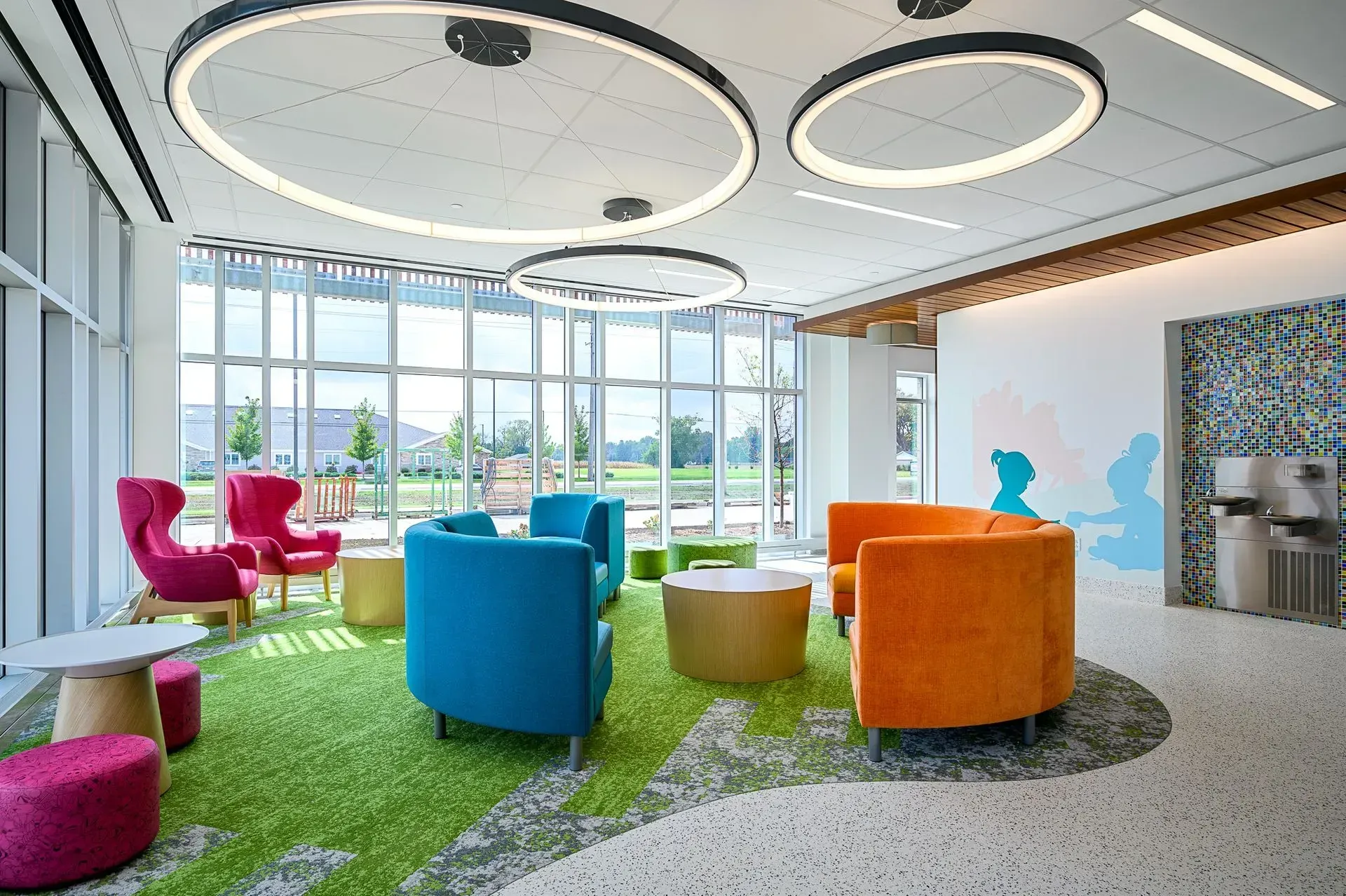 A colorful seating area in a modern building with large windows, circular lights, and a green patterned rug.