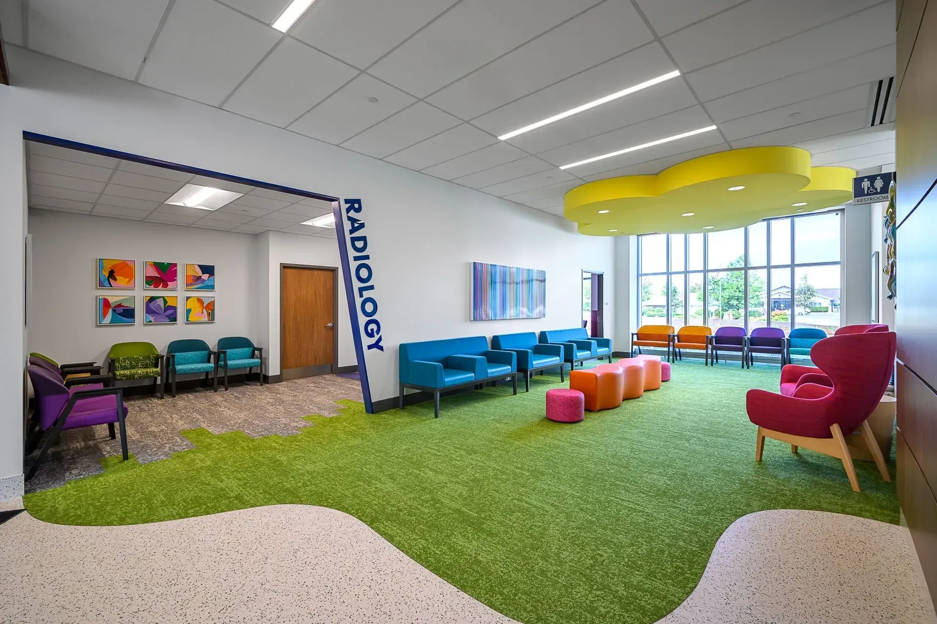 Radiology waiting area with colorful seating, artificial grass, and cloud-shaped ceiling fixture.