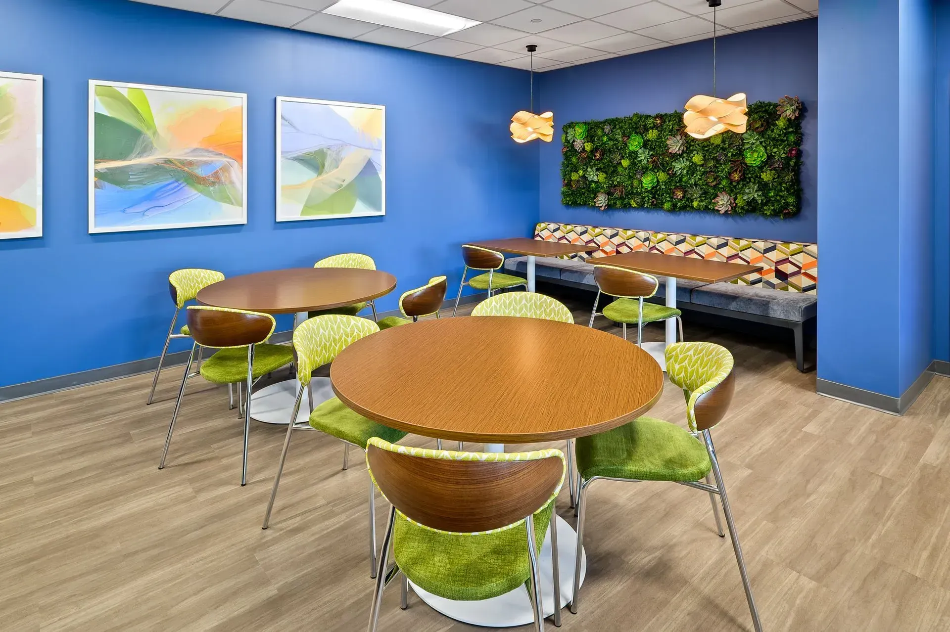 Modern break room with blue walls, round tables, green chairs, and a plant wall.