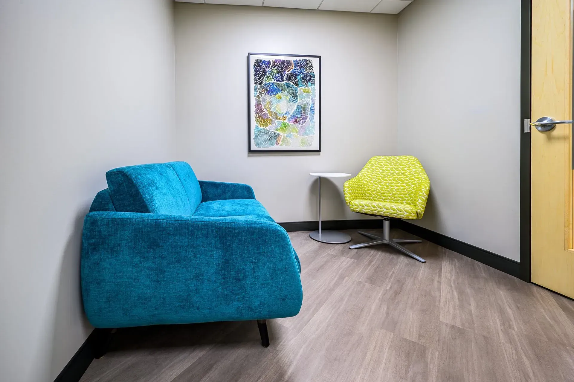 Cozy waiting area with turquoise sofa, lime green chair, abstract art, and small side table.