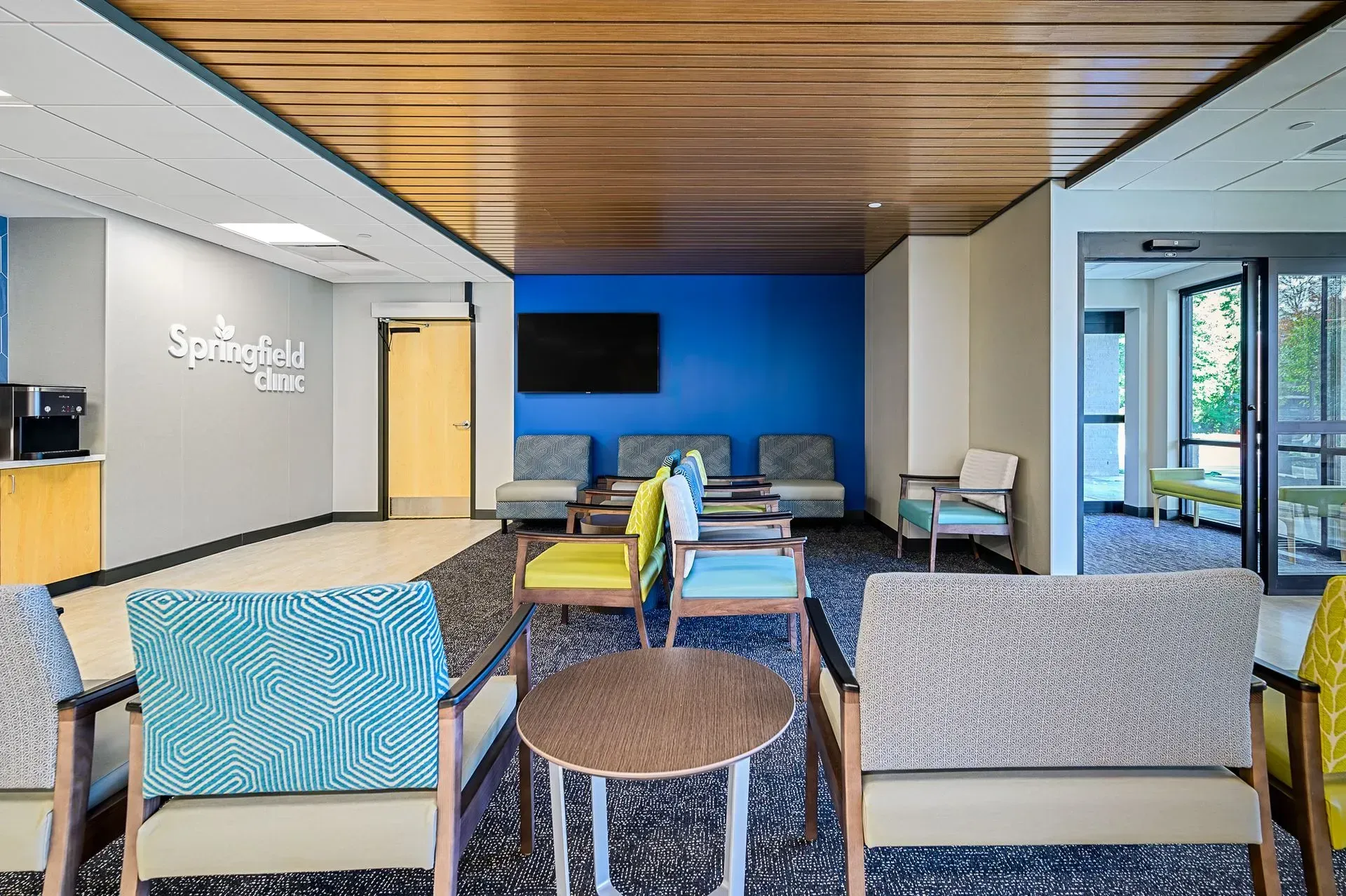 Waiting room with patterned chairs, blue wall, wood ceiling, and doorway to outside.