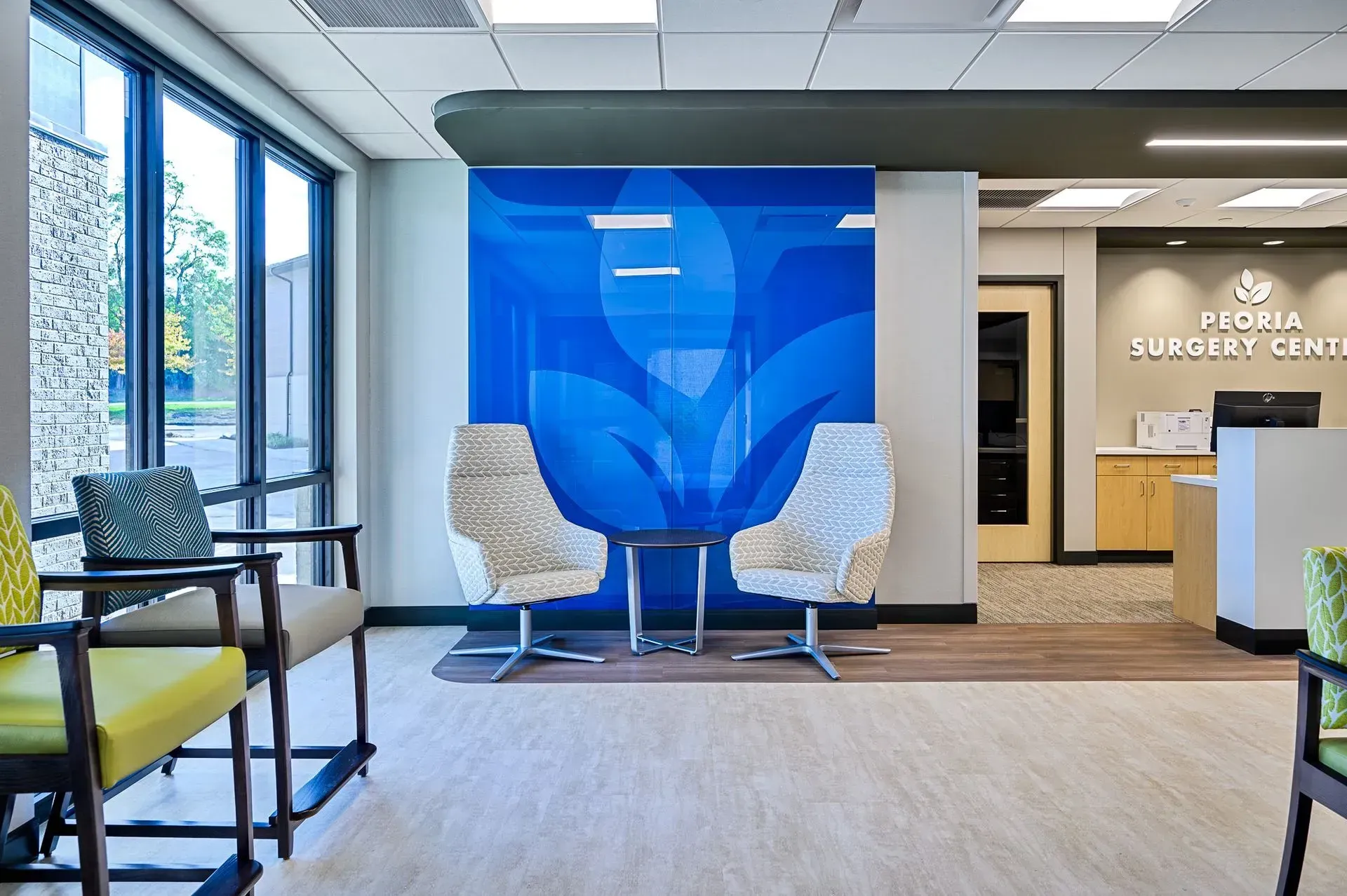 Waiting room at Peoria Surgery Center; blue wall art, beige chairs, and reception desk.