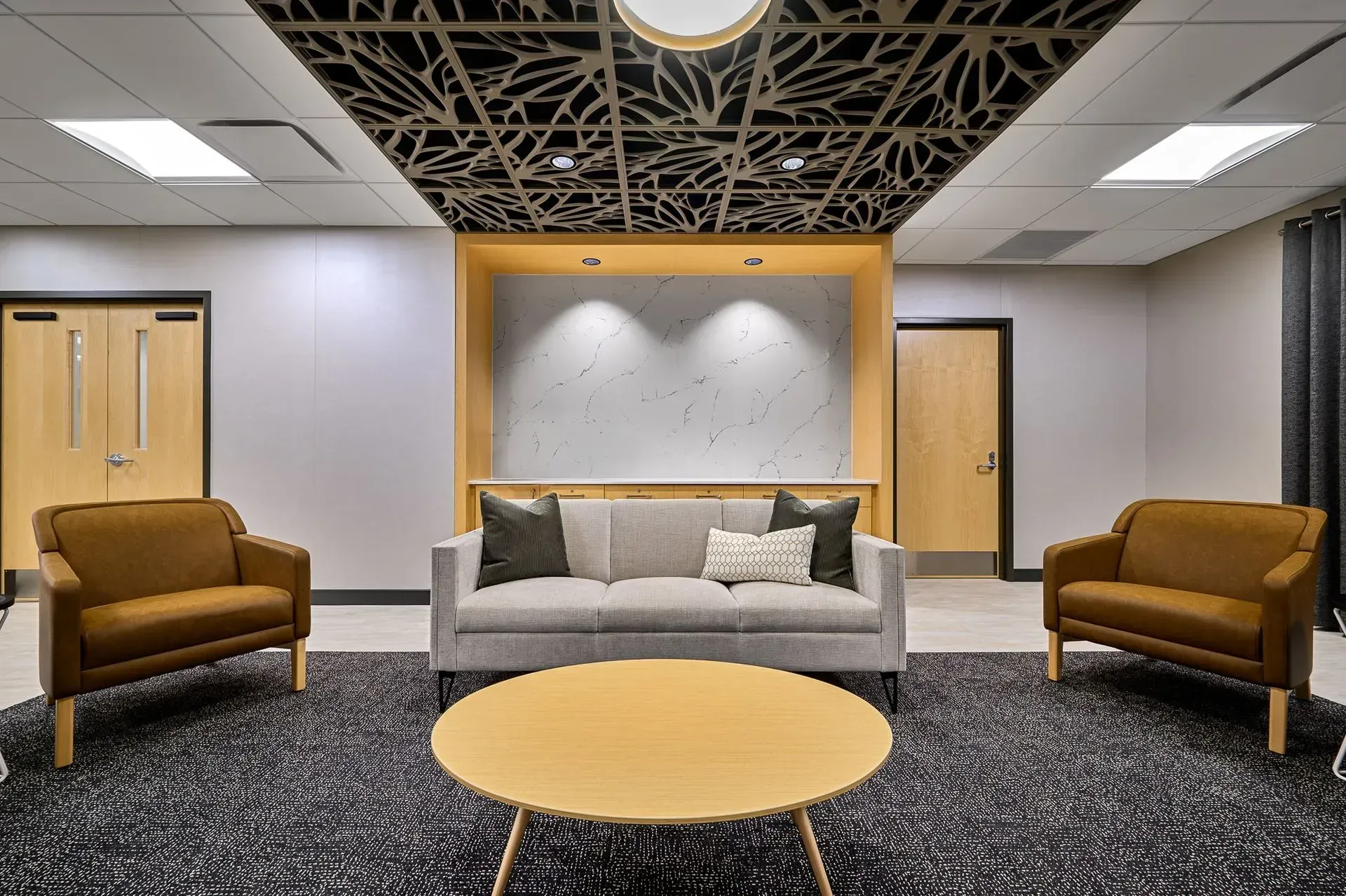 Lounge area with sofa, chairs, coffee table, patterned rug, and decorative ceiling panels.