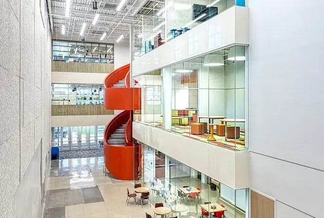 Interior view of a modern building with a bright orange spiral staircase, and glass-walled levels.