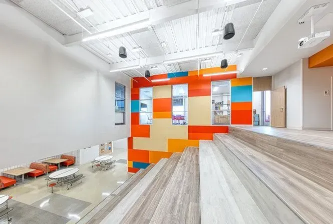 Interior view of modern building with colorful accent wall, staircase, and cafeteria.