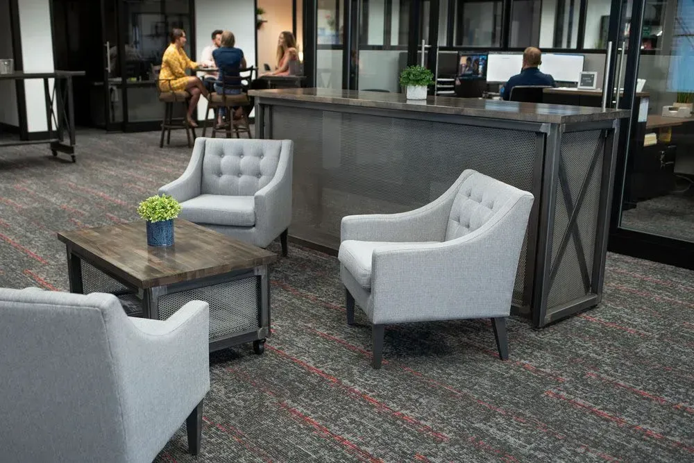 Lounge area with gray chairs, a wooden coffee table, and a metallic bar. People sit in the background.