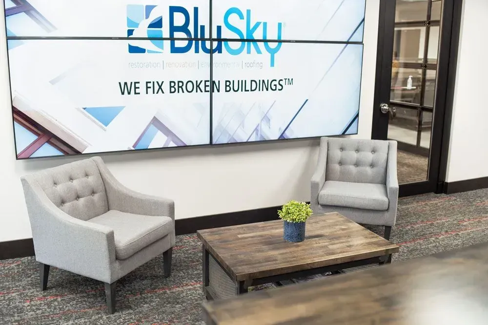 Lobby with two gray armchairs, a wooden coffee table, and a video wall displaying the BluSky logo.
