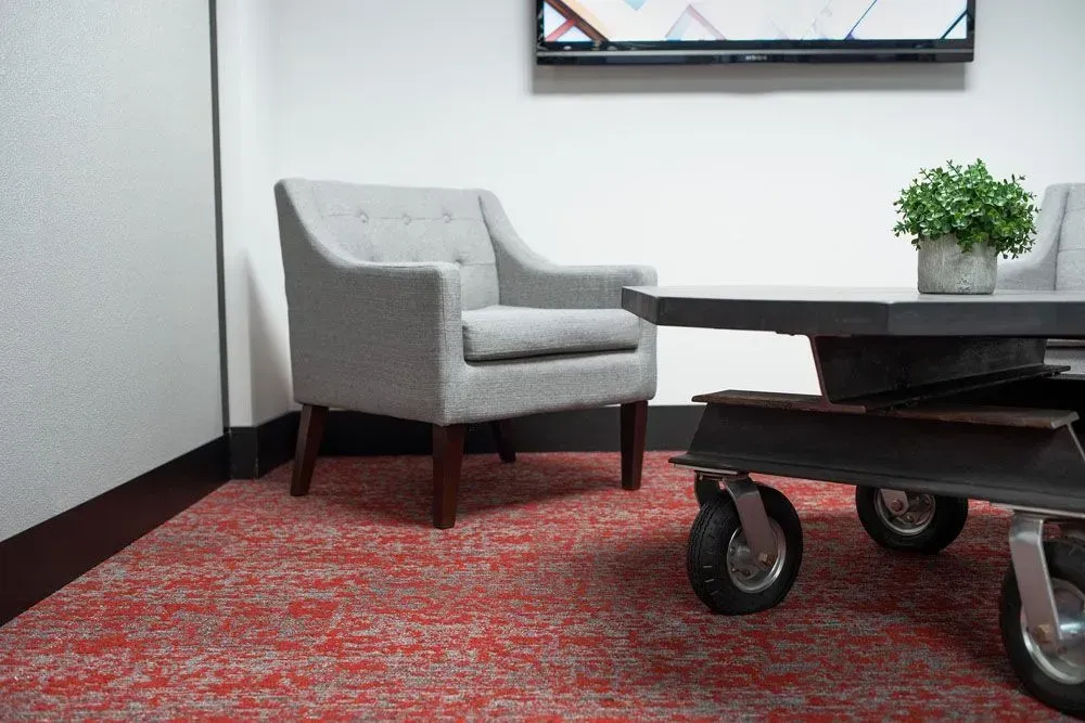 Gray armchair, industrial coffee table, potted plant, red patterned carpet.