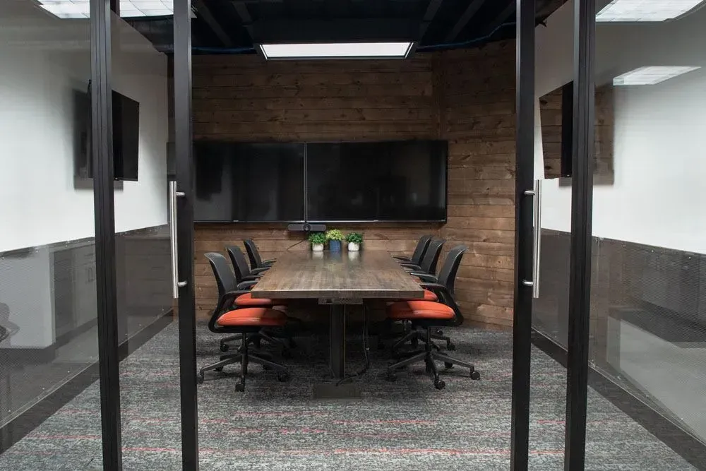 Conference room with a wooden table, chairs, and two screens on a brick wall.