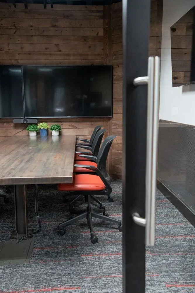 Conference room with long table, black chairs, and large screen. Door handle in foreground.