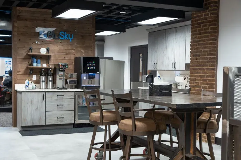 Office kitchen with coffee station, small refrigerator, and a table with bar stools.