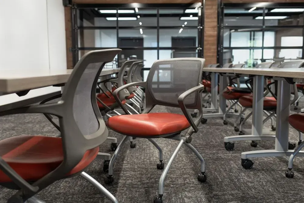 Office chairs with red seats arranged in a classroom setting with tables and windows.