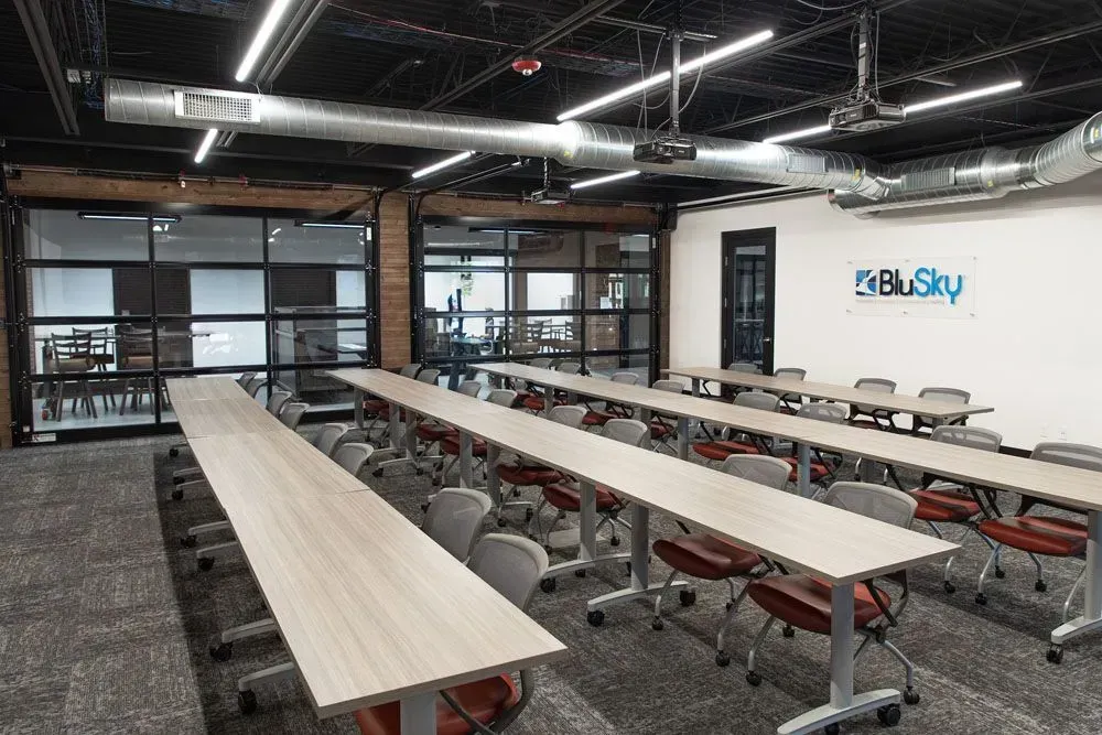 Classroom with long tables, chairs, glass walls, and a logo.