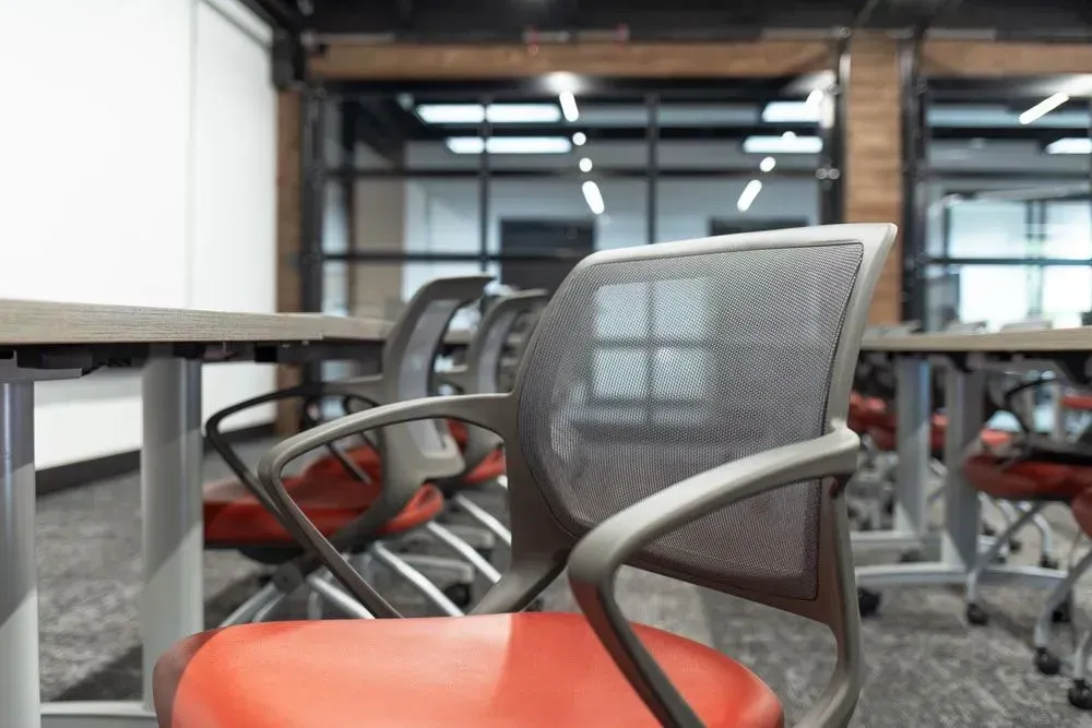 Close-up of a mesh-backed office chair with a red seat at a table, in a modern workspace.