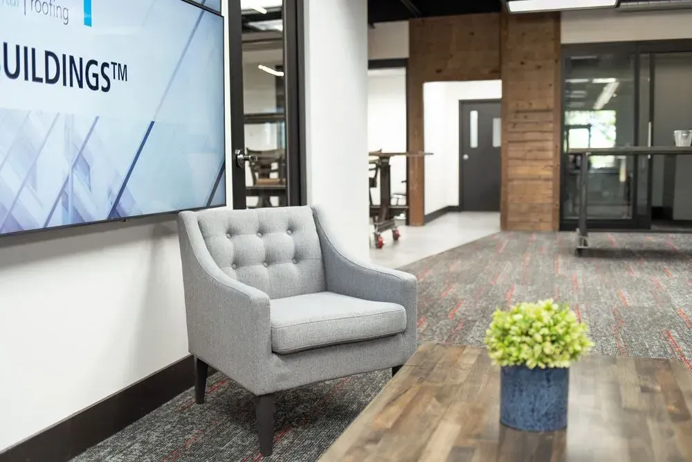 Gray upholstered armchair in a waiting area with a large screen displaying 