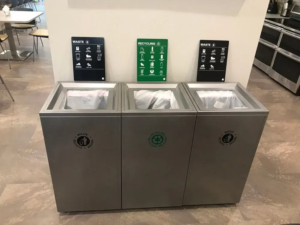 Three recycling bins, labeled for trash, recycling, and compost, with corresponding instructional signs above them.