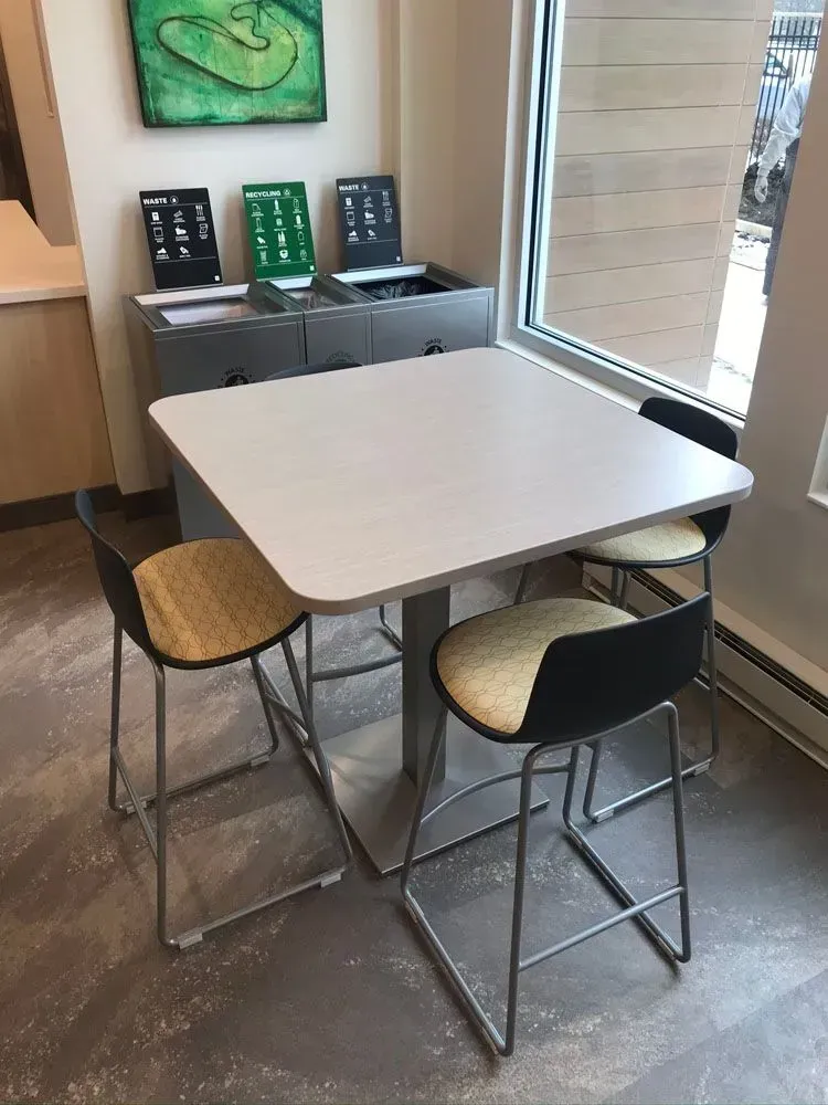 Square table with four bar stools, near a window and a console with electronic devices.