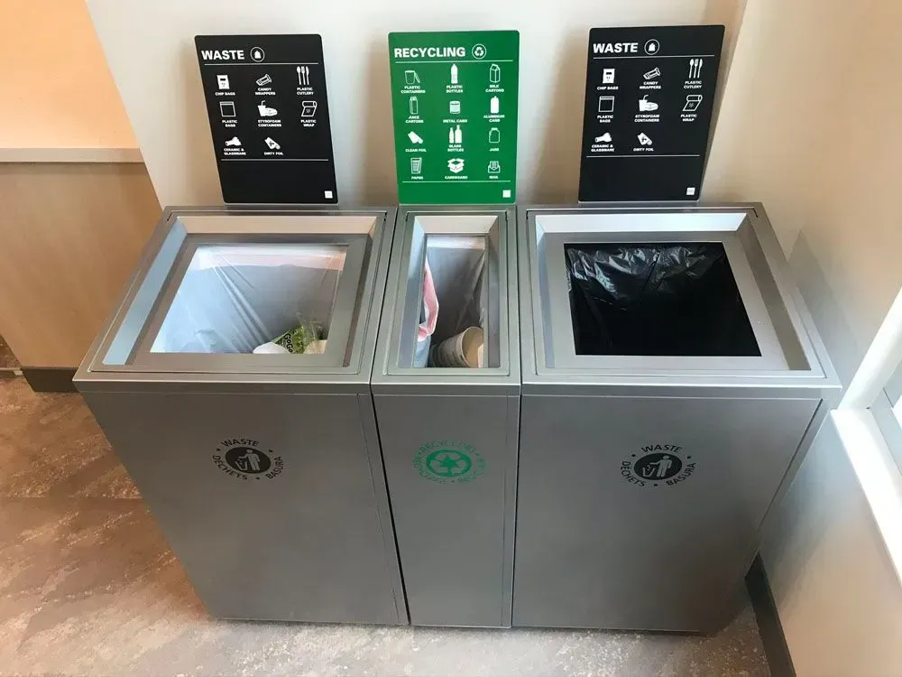 Three silver recycling bins: waste, recycling, and waste, with corresponding signage.