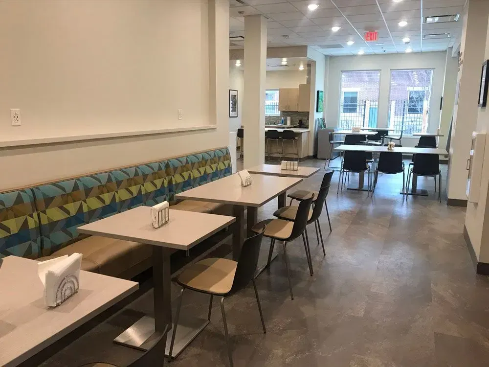 Restaurant seating area with tables, built-in bench, chairs, and kitchen in the background.