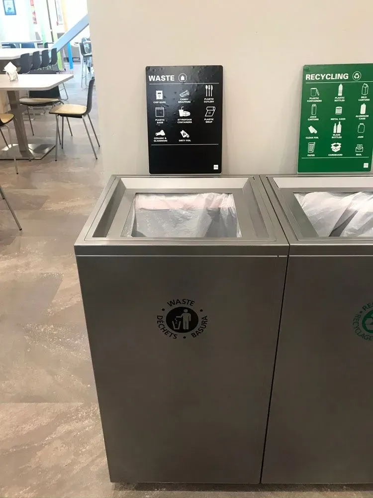 Waste and recycling bins in a public space, with informational signs above.