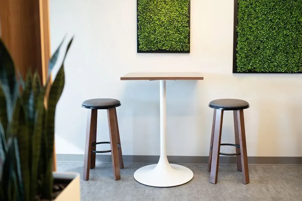 Two wooden stools, white table, and green wall art in a modern interior setting.
