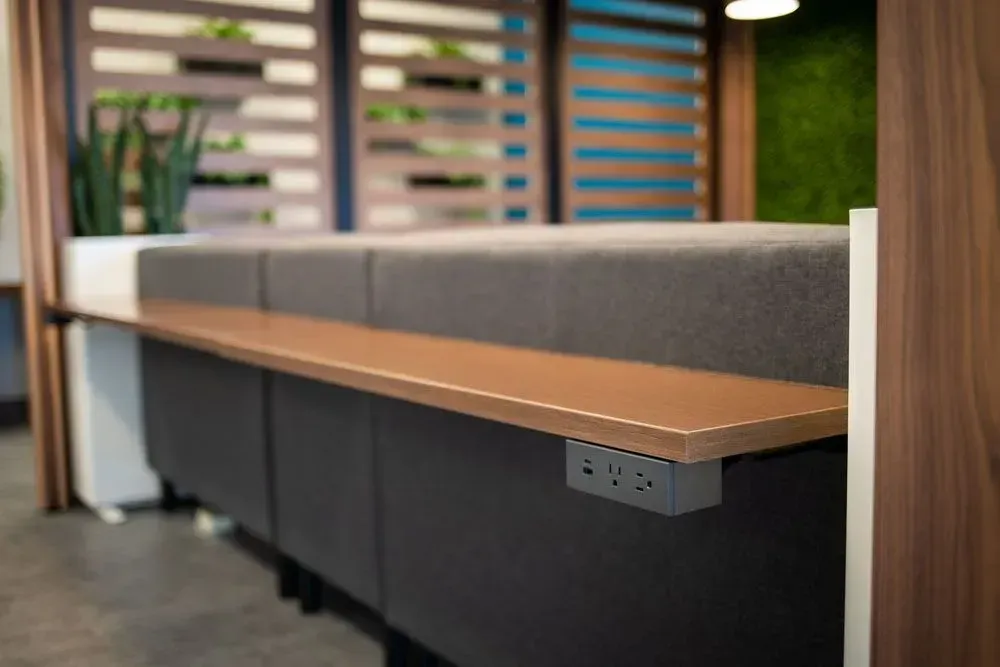 Wooden desk with built-in power outlets and gray padded divider in a modern office.