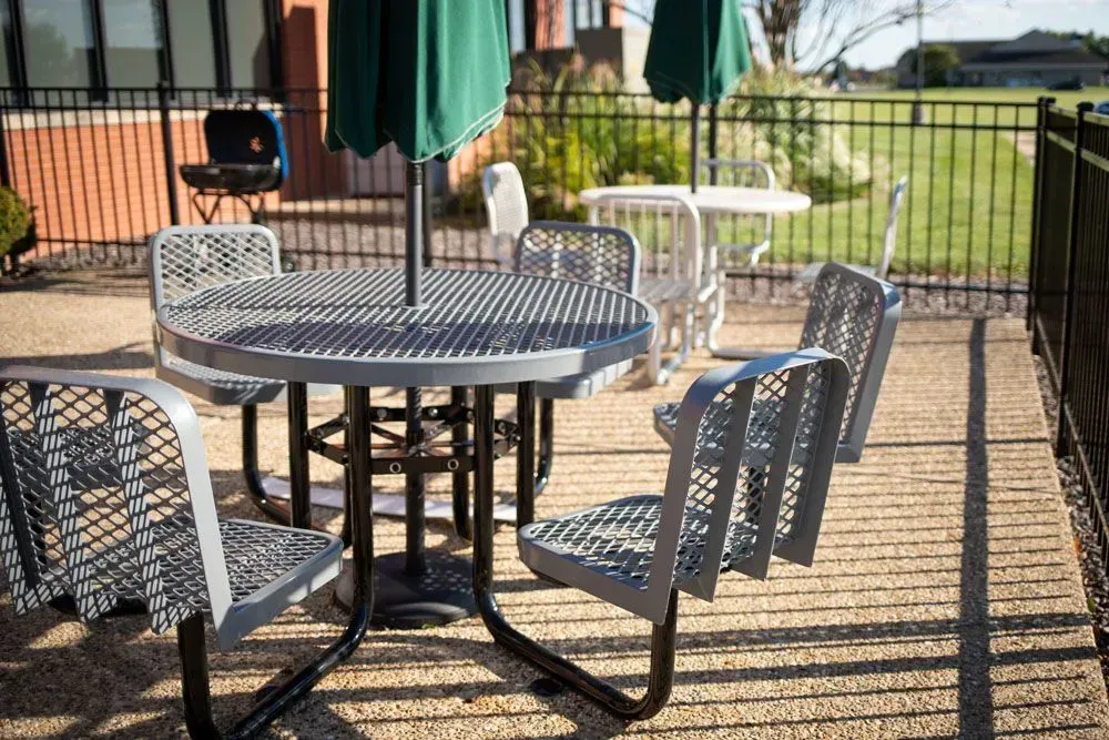 Outdoor seating area with round metal tables, chairs, and green umbrellas.