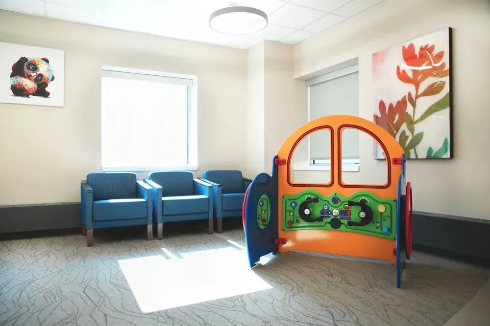 Waiting room with blue chairs, play structure, and artwork.