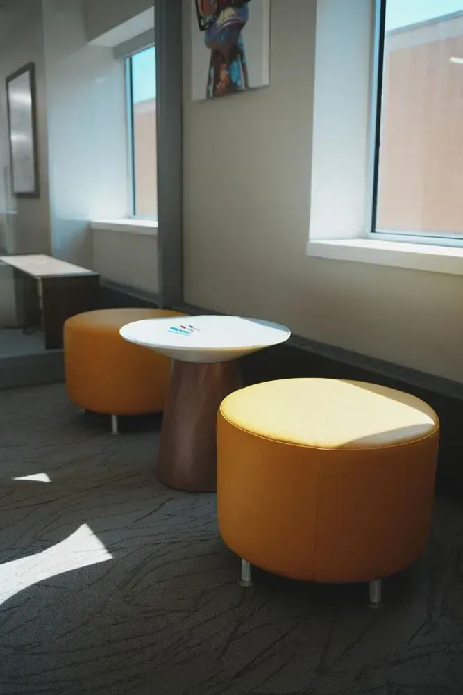 Two orange ottomans and a white table near windows in a waiting area.