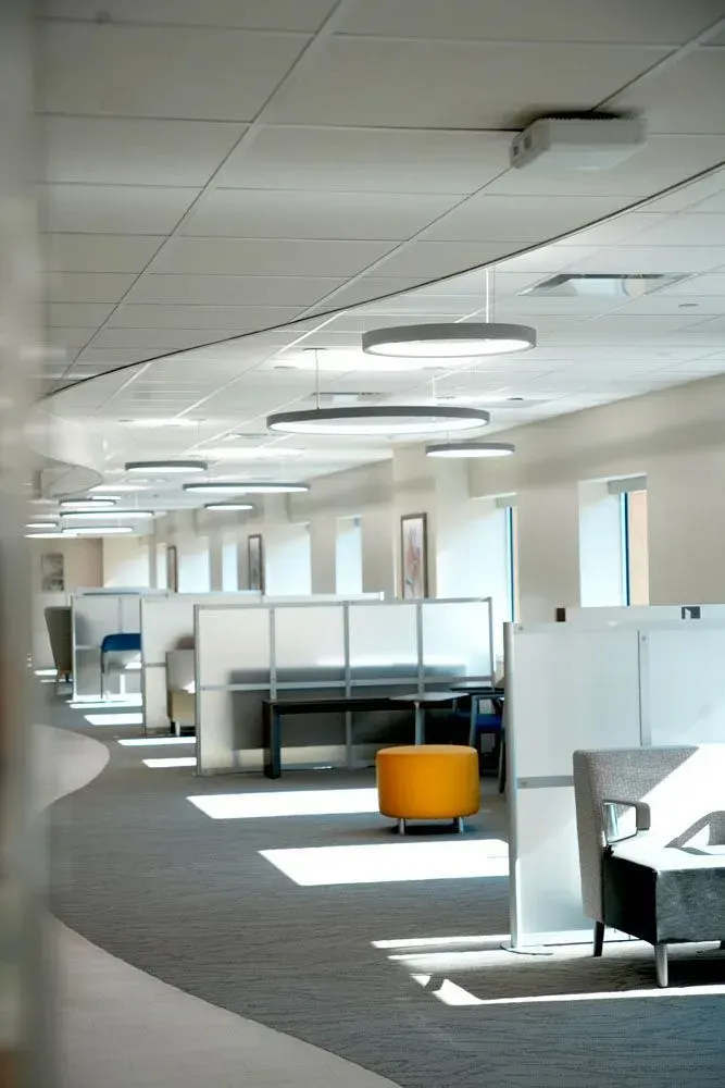 Office cubicles with gray carpet, white walls, and circular hanging lights. An orange stool sits in an aisle.