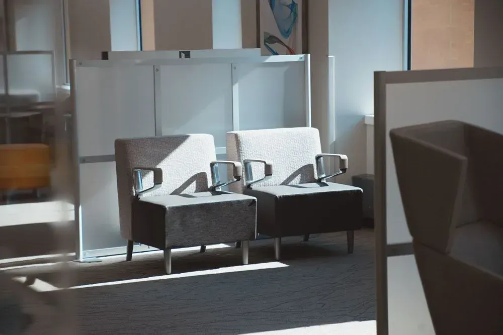 Two armchairs in a bright waiting room with sunlight, next to a window and white storage.