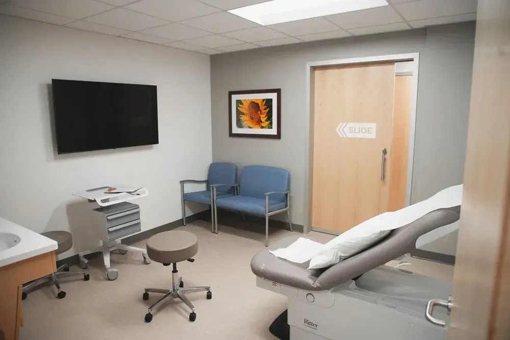 Medical exam room with examination table, seating, and a mounted TV.